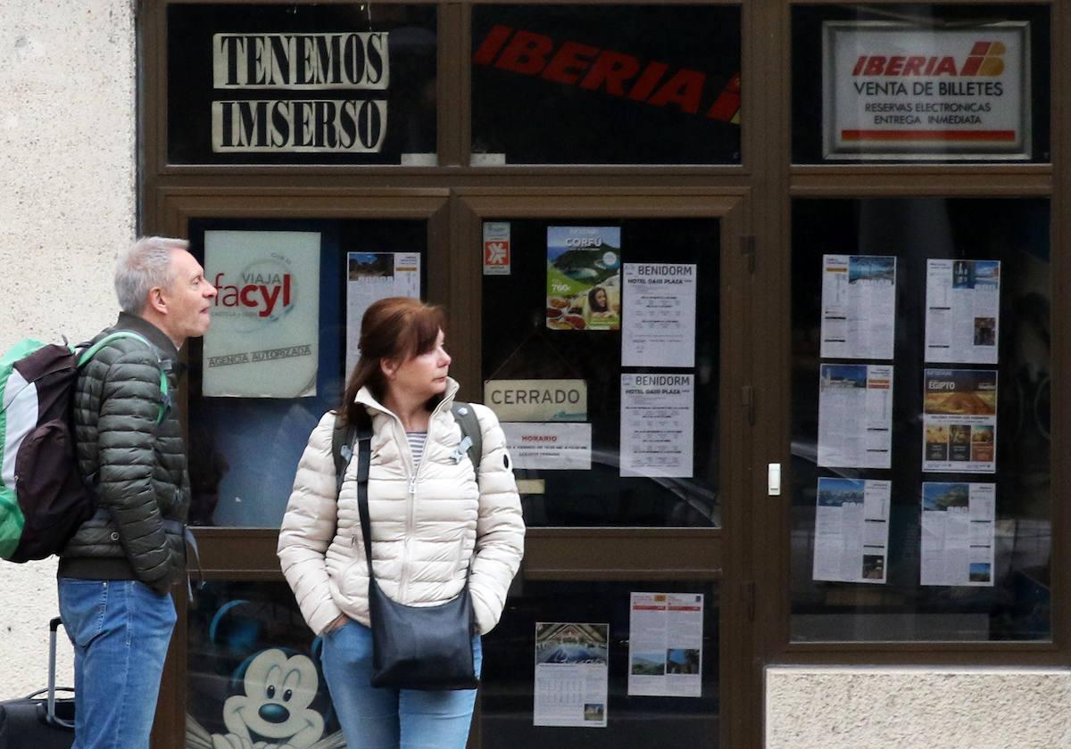 Un hombre y una mujer, junto a una agencia de viajes que ofrece viajes del Inmserso en Segovia.