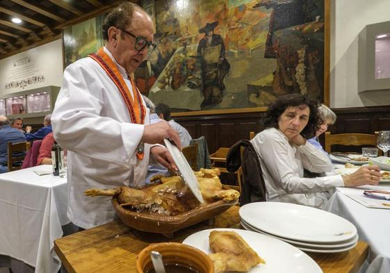 El hostelero Jose María parte con el plato un cochinillo.