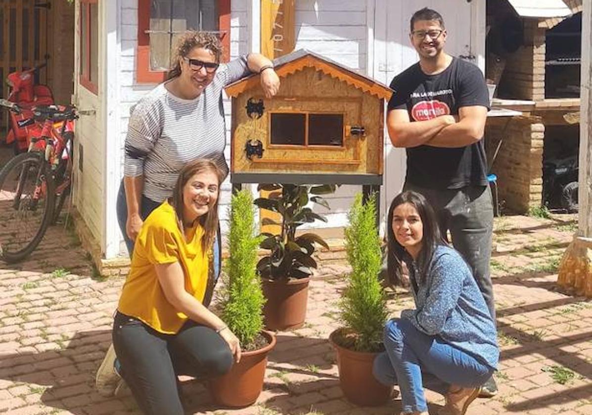 Noelia, Leticia (a la izquierda) y Cinthia, del AMPA de Villalón, y Alberto, el ebanista, posan con la nueva caseta para el intercambio de libros.