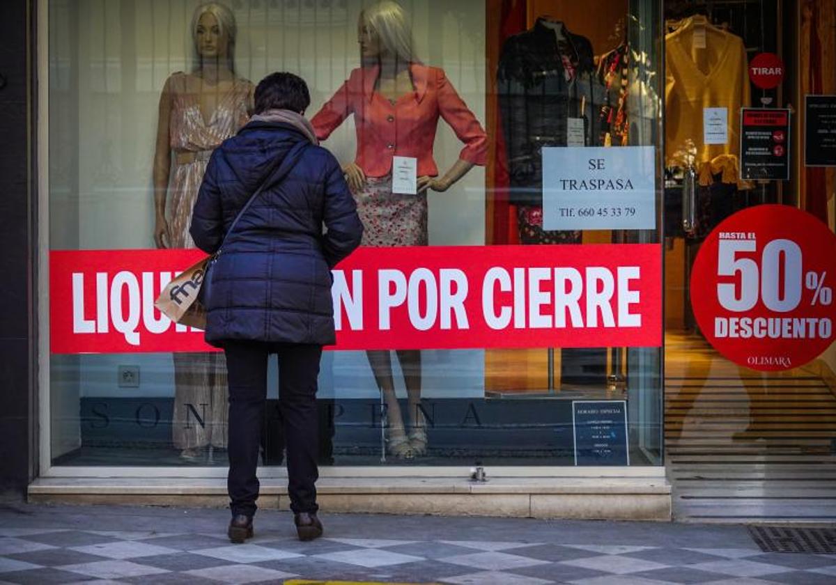 Una mujer mira el escaparate de un comercio en liquidación.