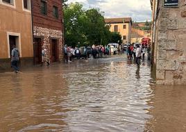 Vecinos tratan de sortear una balsa de agua y barro en Ayllón tras la tromba de este domingo.