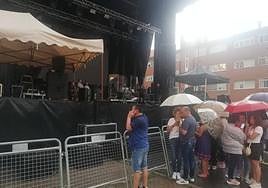 Vecinos se protegen con paraguas de la tormenta ante el escenario donde actuará Camela esta noche.