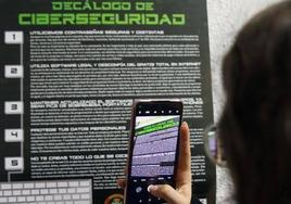 Una persona hace una fotografía de un cartel de recomendaciones sobre ciberseguridad.