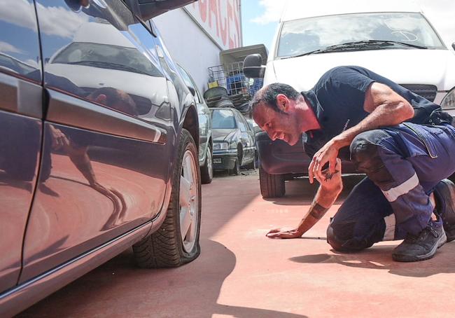 Alfredo Mangas, del taller Las Torres, inspecciona un coche con las ruedas desinfladas.