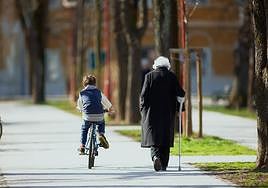 Una persona mayor camina junto a un niño en bicicleta.
