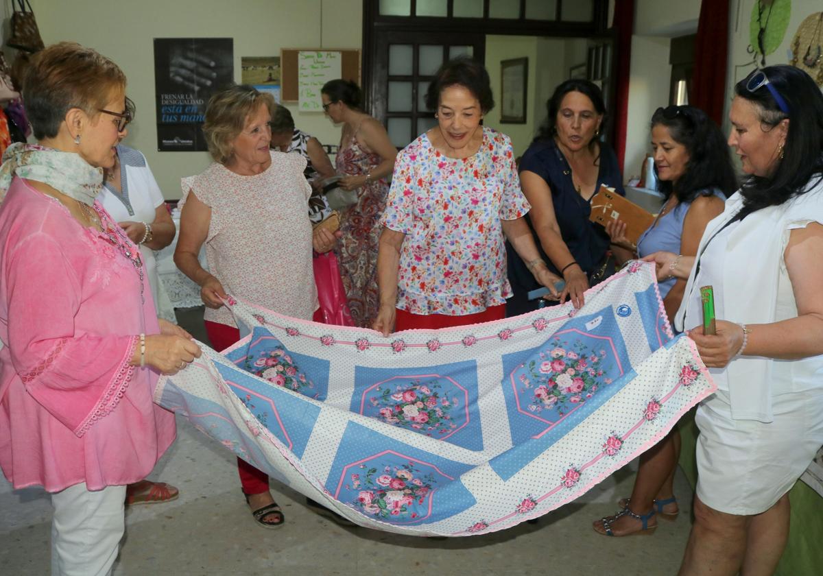 La alcaldesa, Sara Esteban, con varias mujeres voluntarias, muestran un mantel artesanal.