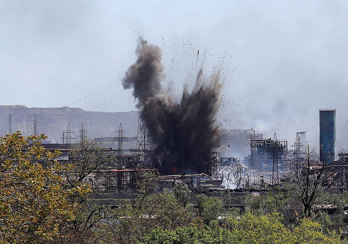 Imagen principal - Una bomba estalla durante el asedio ruso a la planta. Dos Soldados caminan sobre el entramado de hierros en el que se convirtió la acería tras los ataques.