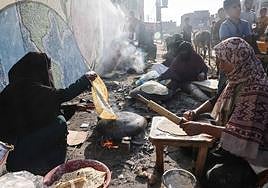Mujeres palestinas hornean pan sobre fuego de leña en un refugio para familias desplazadas del norte de la Franja de Gaza.