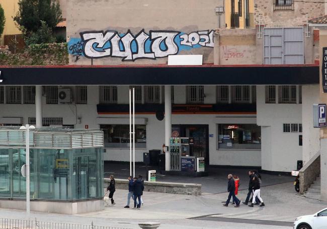 Varias personas pasean cerca de la gasolinera coronada por una pintada.