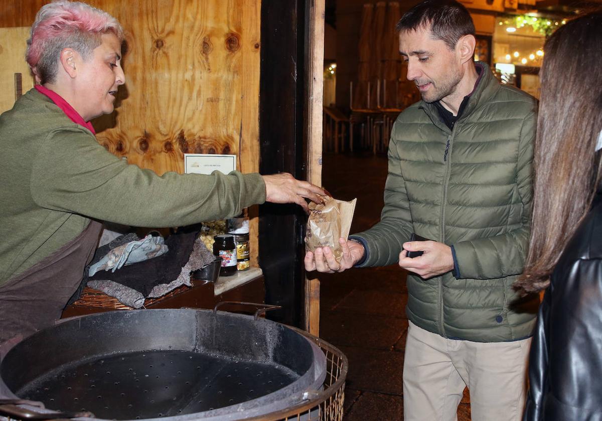 La castañera Gloria Rodera vende una bolsa de castañas asadas a un hombre, en su puesto en la Calle Real.