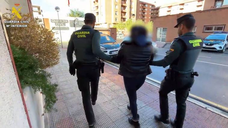 La madre detenida, esposada, es escoltada hasta un vehículo por dos guardias civiles.