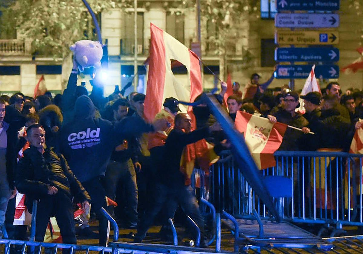 Varios jóvenes destrozan las vallas de seguridad que les separan de la policía, durante una manifestación contra la amnistía frente a la sede del PSOE en Ferraz.
