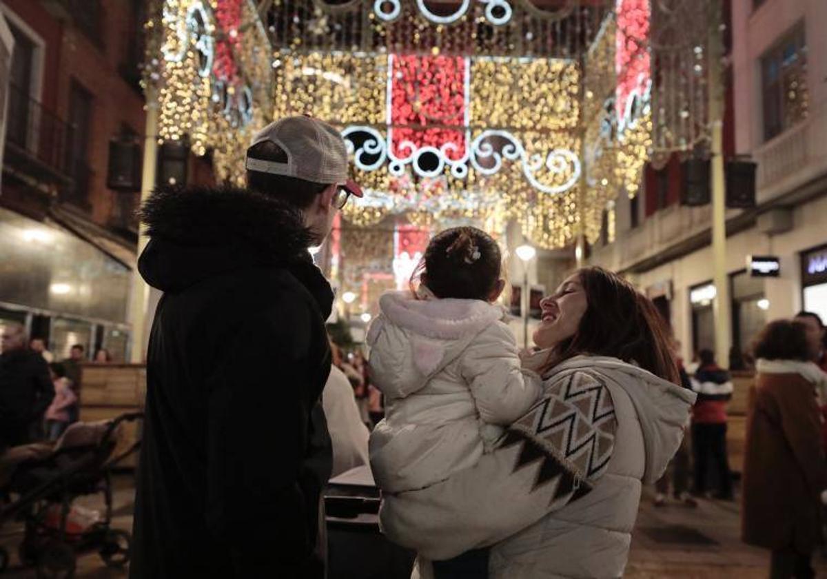 Una pareja mira las luces navideñas de la calle Santiago con un niña en brazos.