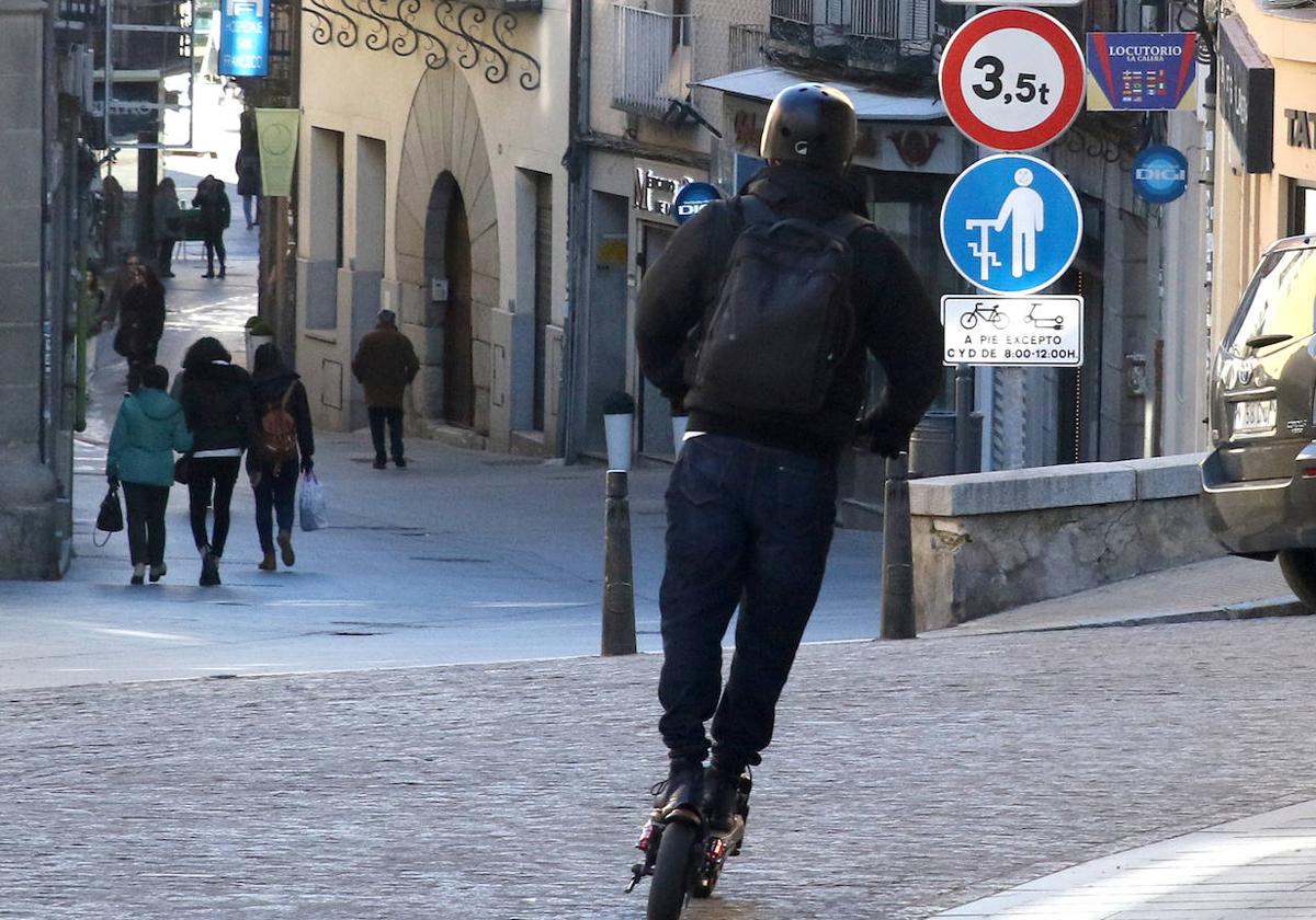 Un joven cruza en patinete una calle segoviana.