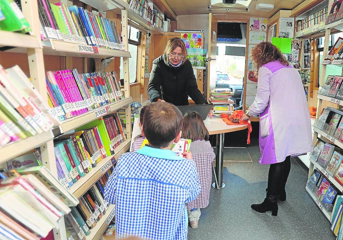 Asun Méndez prepara libros junto a una maestra y varios niños en un bibliobús en Magaz de Pisuerga (Palencia).