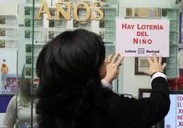 Colocación de un cartel que anuncia la venta de Lotería del Niño en Segovia, este viernes por la mañana.