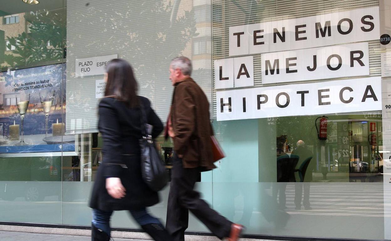 Dos personas pasan ante la sede de un banco con un anuncio hipotecario. 