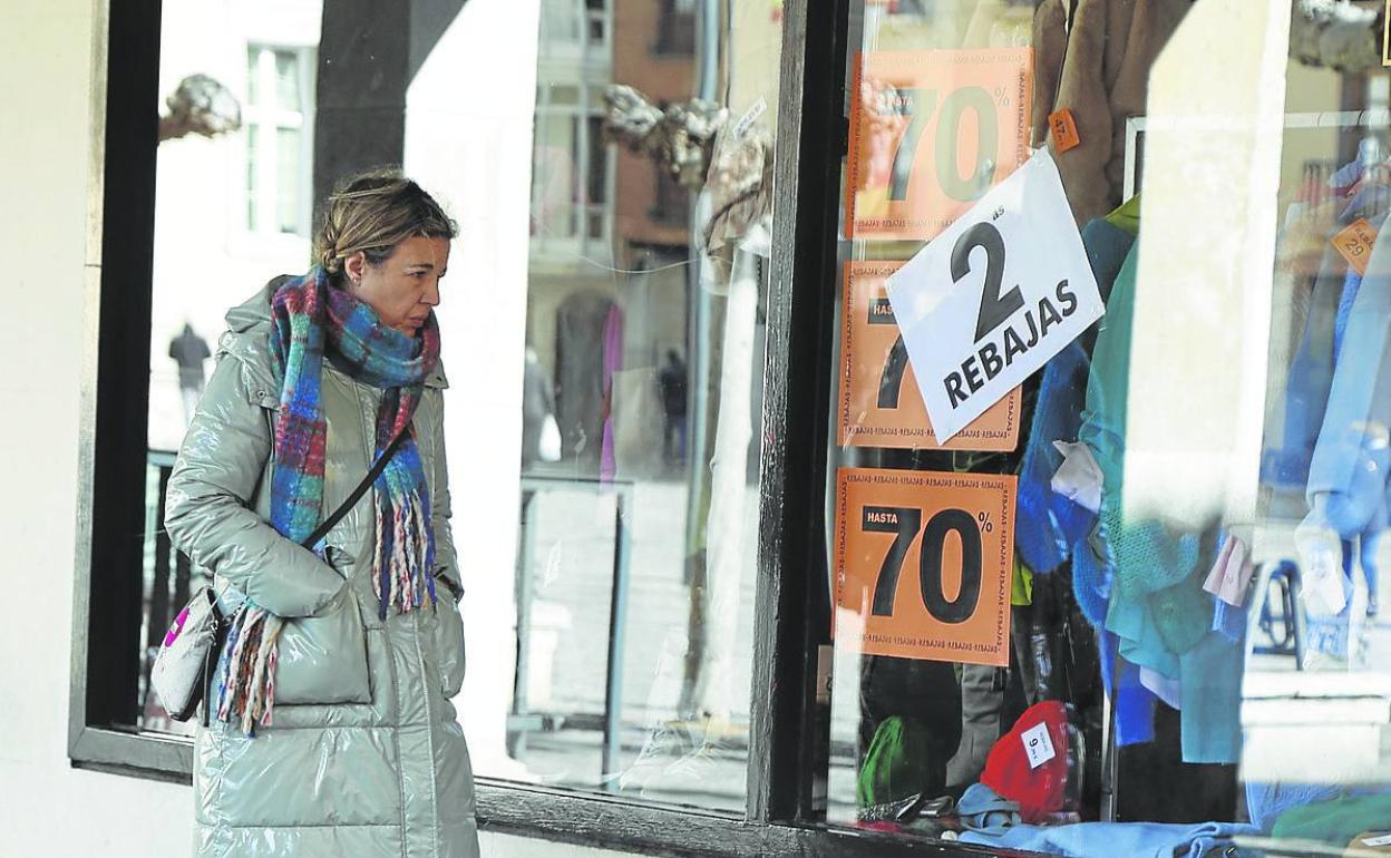 Una joven pasa junto a un escaparate con los carteles de rebajas.