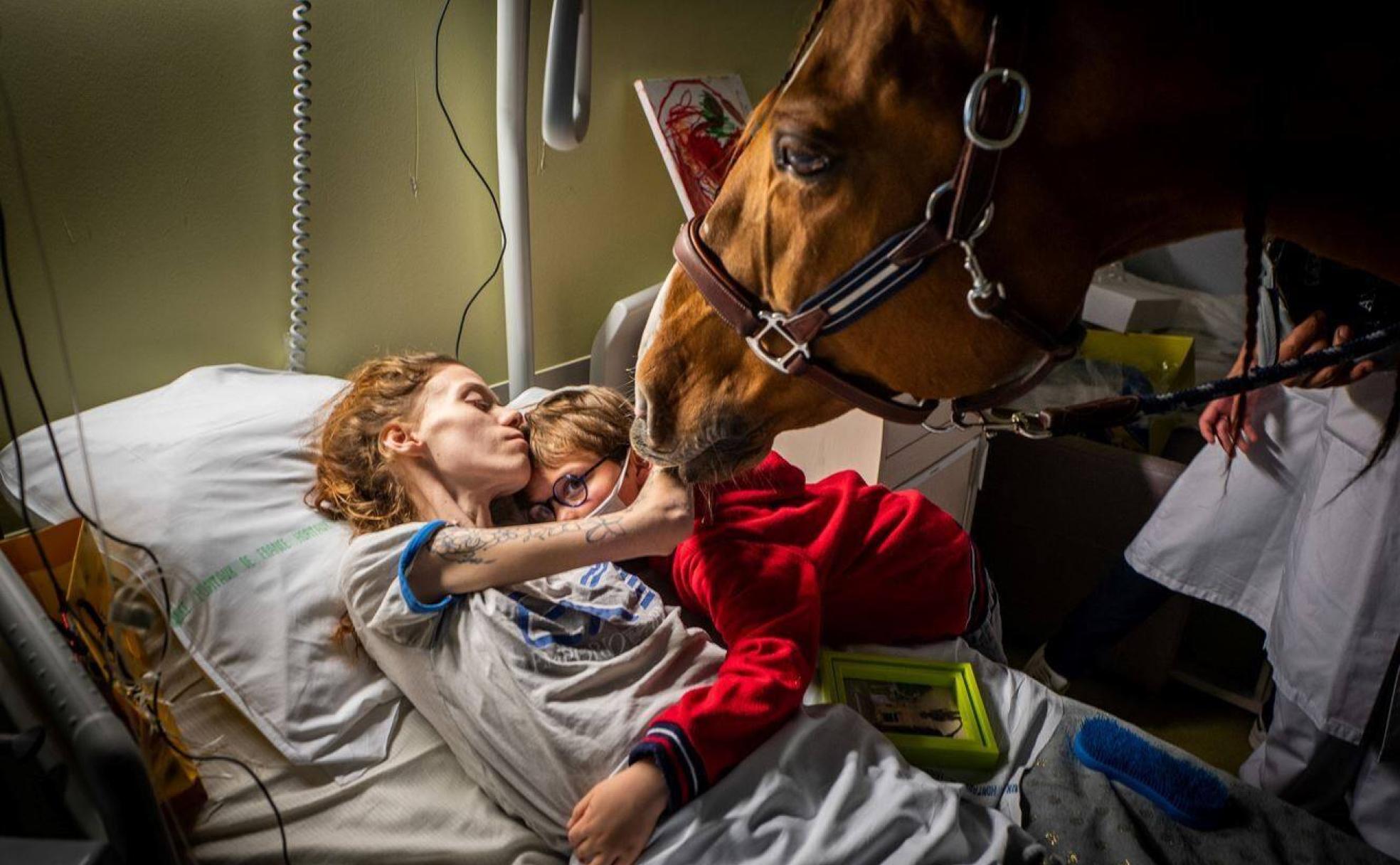Marion, de 24 años y con cáncer metastásico, abraza a su hijo Ethan y acaricia a Peyo, un caballo que forma parte de las terapias paliativas de un hospital de Calais. 
