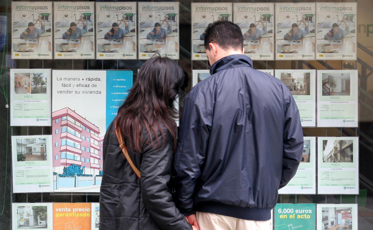 Una pareja compara precios frente al escaparate de una inmobiliaria. 