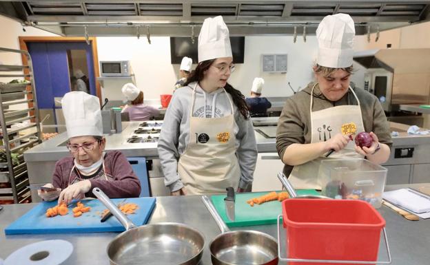 Tres alumnas cortan verduras en el curso para hacer la receta de lentejas. .