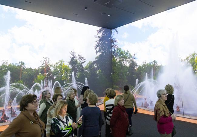 Visitantes en el cubo inmersivo, rodeados de escenas proyectadas de los jardines y las fuentes de La Granja de San Ildefonso.