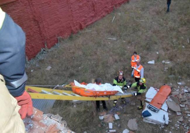 Los bomberos y forenses rescatan el cadáver de Teresa por la parte trasera del inmueble.