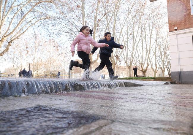 Dos menores saltan el agua que brotaba del reventón en el paseo del Cauce.