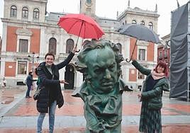 Dos mujeres protegen con sus paraguas la estatua de los Goya en la Plaza Mayor.