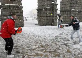 Dos jóvenes juegan al pádel bajo la nieve con el Acueducto de fondo.