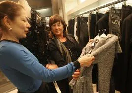 Una clienta mira una prenda en una tienda de moda junto a la dependienta.