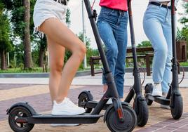 Tres jóvenes con sus patinetes eléctricos en un parque.