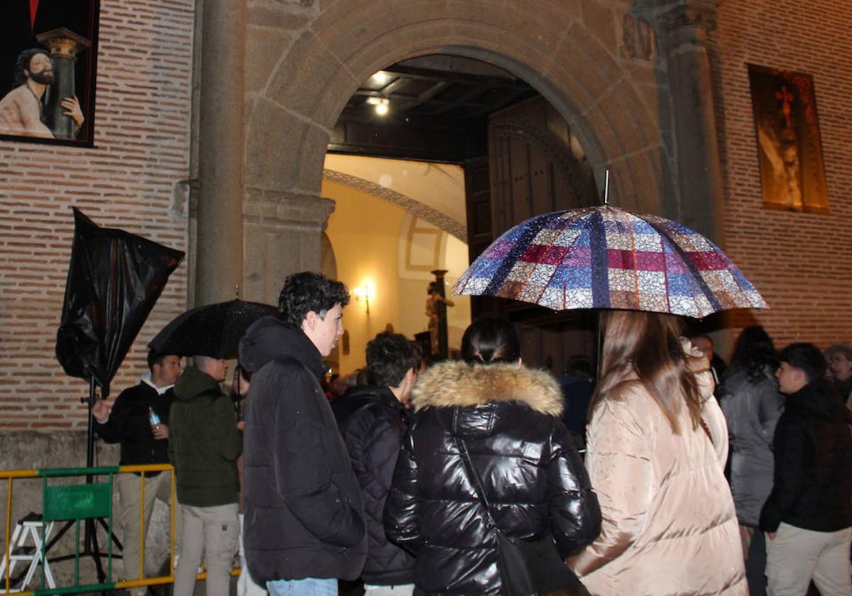 Varias personas, tapadas con paraguas en la puerta de la iglesia tras la suspensión de la Procesión de la Caridad.