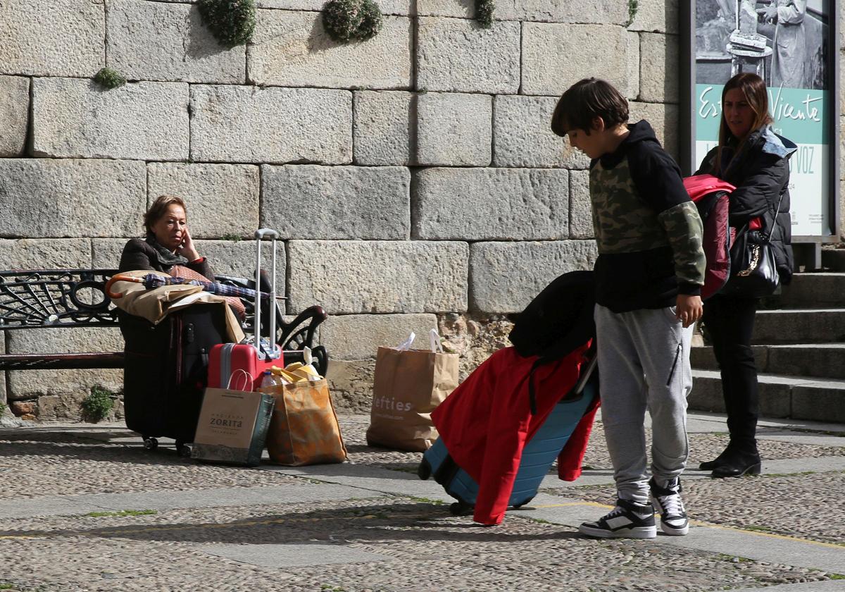 Varias personas esperan con maletas en el centro de la ciudad de Segovia.