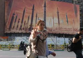 Una mujer hace el gesto de la victoria delante de un cartel de propaganda bélica en Teherán.
