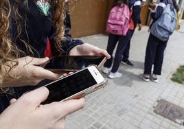 Varios jóvenes, con el móvil a la entrada de un instituto.