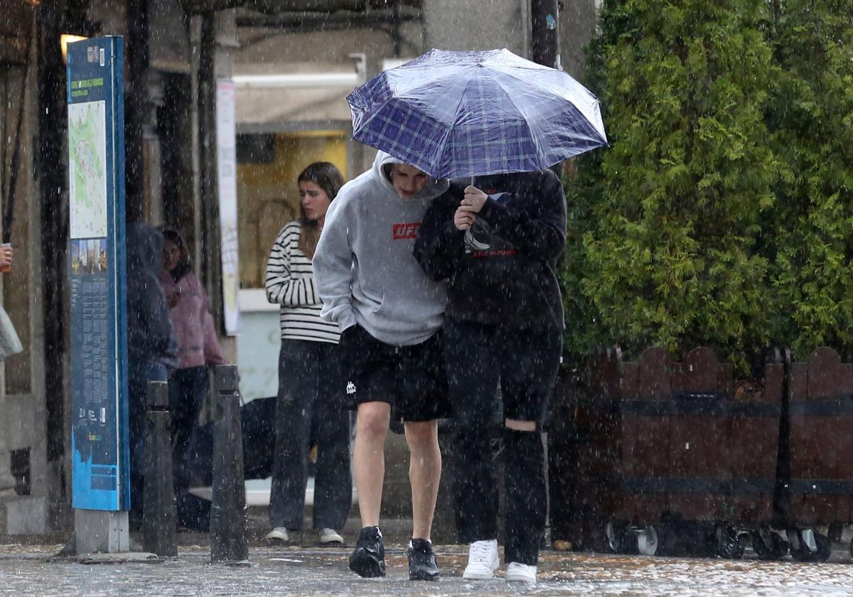 Dos jóvenes se protegen de la lluvia en Segovia, hace unos días.