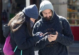 Dos personas abrigadas observan su teléfono móvil.