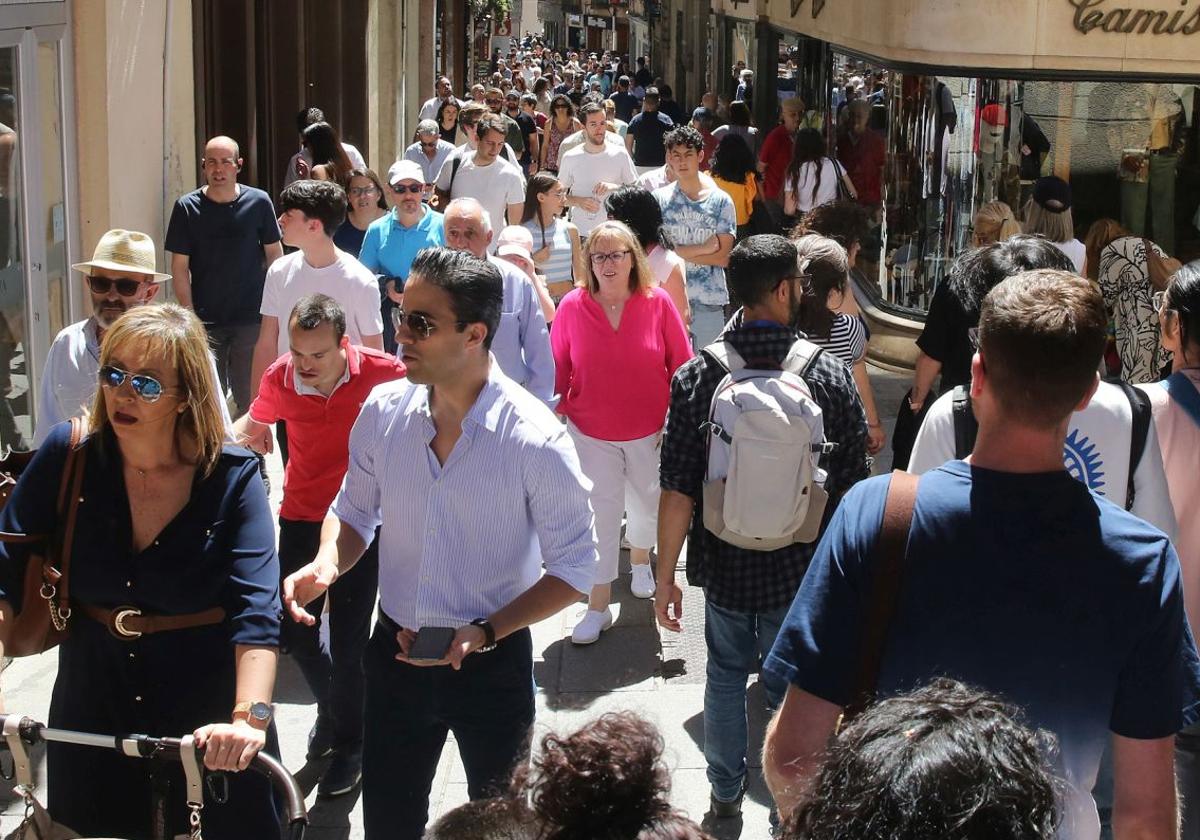 Denas de personas pasean por la Calle Real de Segovia en un día soleado.