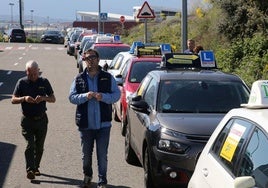 Dos hombres pasean junto a vehículos de autoescuela aparcados en la ciudad de Segovia.