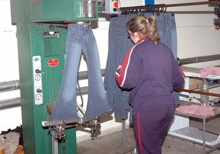 Una joven trajadora ajusta unos pantalones vaqueros en una fábrica textil.