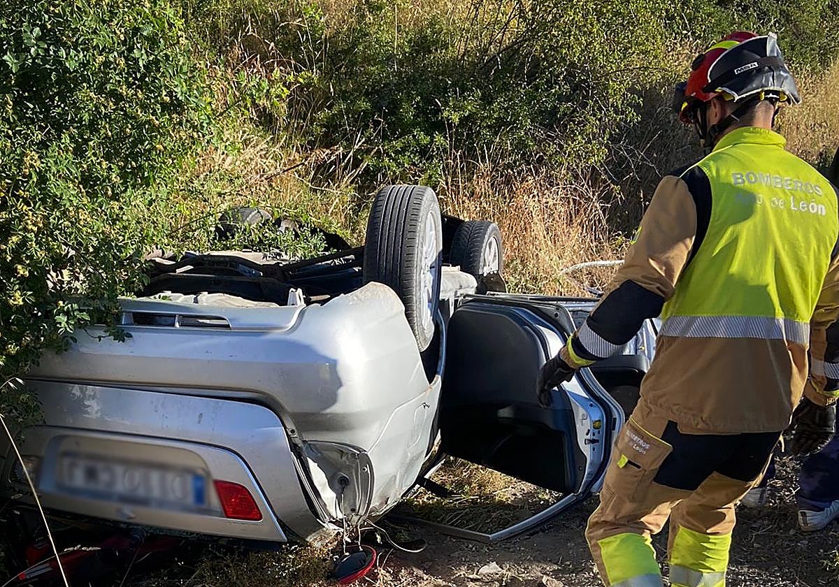 Un miembro de los Bomberos de León, junto al vehículo volcado.