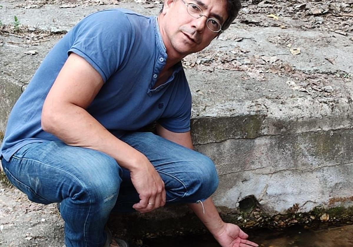 Carlos Calvo, alcalde de Carbonero de Ahusín, mete la mano en el agua del manantial.