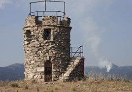 Torre de Cabeza Reina, este jueves sin vigilancia presencial, y al fondo el humo del incendio en la garganta del río Moros.