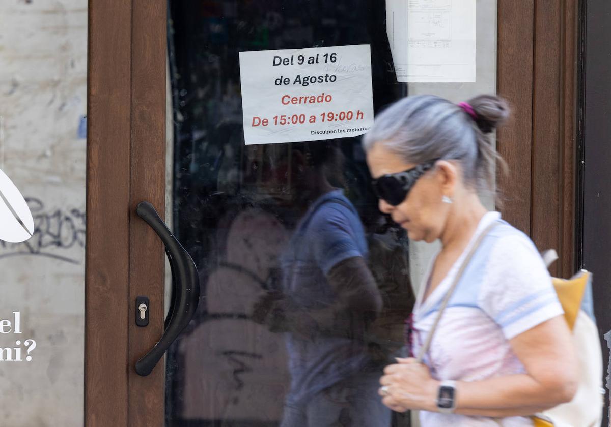 Una mujer pasea delante de un negocio cerrado con un cartel que avisa del horario de tarde del verano.