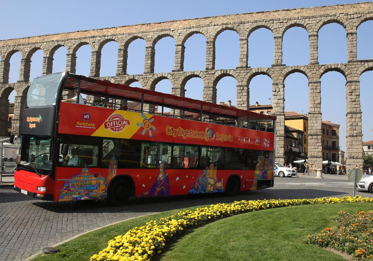 El autobús turístico de Segovia circula delante del Acueducto.