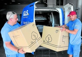 Dos repartidores descargan cajas de un vehículo eléctrico.