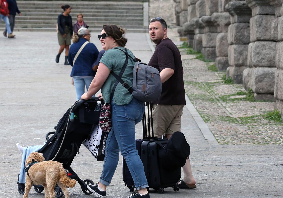 Dos turistas cruzan el Azoguejo con sus maletas.