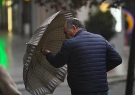 Un hombre intenta sujetar su paraguas por el viento en Valladolid.