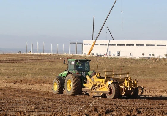 Un tractor trabaja en los terrenos de la urbanización del polígono de Los Hitales, y al fondo las obras de la planta de Drylock.